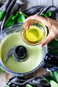 someone pouring olive into a blender filled with green liquid