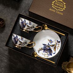 two cups and saucers in a box with gold trimmings on the sides