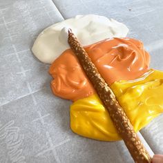 a person holding a stick in front of some food on a table with white and orange icing