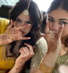 two women with henna on their hands and one holding her hand up to the camera