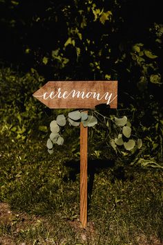 a wooden sign that says ceremony on it in front of some grass and bushes at night