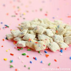 sprinkles and confetti are scattered on a pink surface with white frosting