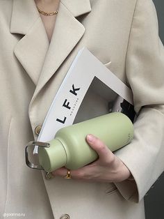 a woman in a beige coat holding a green cup and a white box with the word life on it