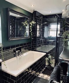 a black and white tiled bathroom with a bathtub, sink, mirror and plants