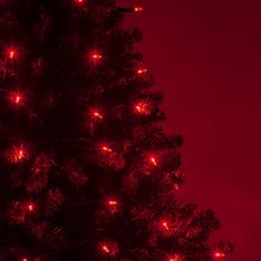 a large christmas tree with red lights on it's branches in front of a red sky