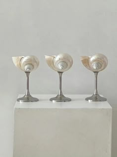 three silver candlesticks sitting on top of a white pedestal with shells in them