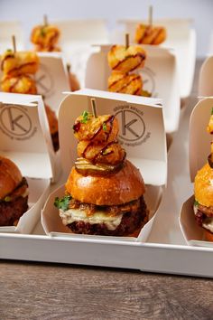 several burgers with onion rings on them are arranged in small white trays for display