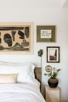 a bed with white sheets and pillows in a bedroom next to pictures on the wall