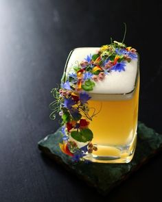 a glass filled with liquid and flowers sitting on top of a green plate next to a black table