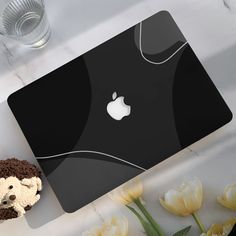 an apple laptop computer sitting on top of a table next to flowers and a cup