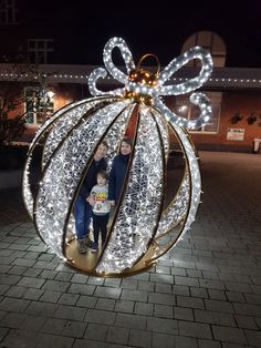 two people and a child standing in front of a christmas ball with lights on it