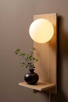 a light that is on the wall next to a vase with a plant in it