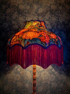 a colorful lamp with fringes on it in front of a wallpapered background