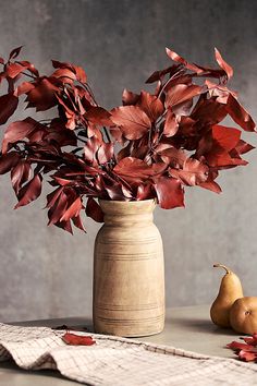 a vase filled with red leaves next to two pears and a napkin on a table