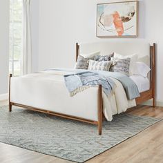 a white bed sitting on top of a wooden floor next to a window in a bedroom