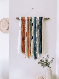 a wall hanging with several different colors of scarves on it next to a plant