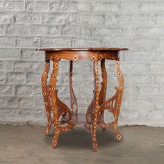 a small wooden table with studded legs and an open drawer on one side, against a white brick wall