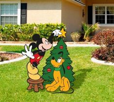 mickey mouse and pluto around a christmas tree in front of a house with landscaping on the lawn