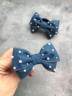 someone is holding two denim bows with white pearls on the ends and one in the middle