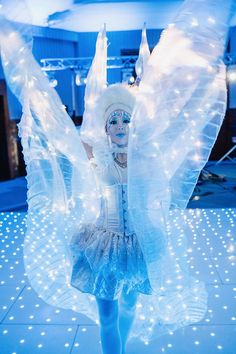 a woman dressed as an angel standing on top of a floor covered in white lights