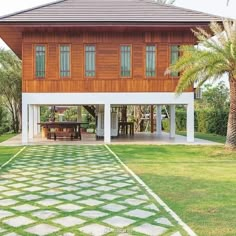 a large wooden house sitting in the middle of a lush green field next to palm trees