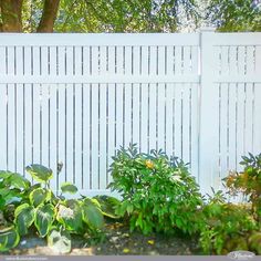 there is a white fence and some plants in front of the bushes on the side of the road