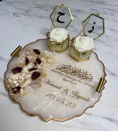 two white roses are sitting on top of a glass plate with gold trimmings