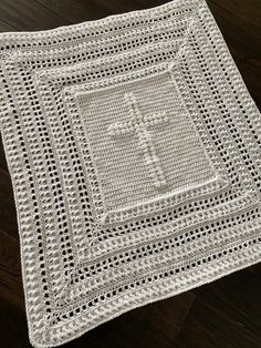 a white crocheted blanket with a cross on the front and center, sitting on top of a wooden floor