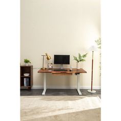 a desk with a computer, lamp and bookshelf in front of a white wall