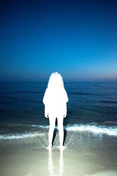 a person standing on the beach looking out at the ocean with their back to the camera