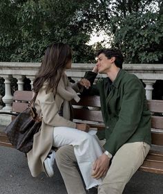 a man and woman sitting on a park bench talking to each other while holding hands