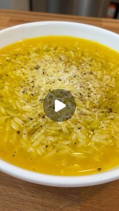 a white bowl filled with yellow soup on top of a wooden table