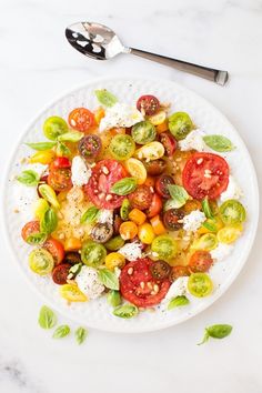 a white plate topped with lots of different types of vegetables next to a fork and knife