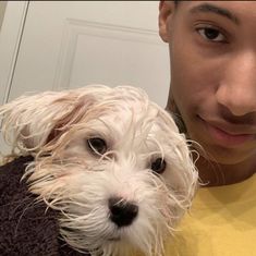 a man holding a white dog in his arms and looking at the camera while wearing a yellow shirt