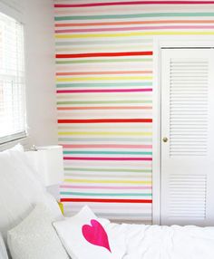 a white bed sitting in a bedroom next to a wall with colorful stripes on it