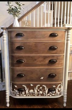 an old dresser has been painted with white paint and flowers on the bottom drawer, along with a vase filled with greenery