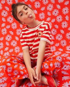 a young boy sitting on top of a red and white flowered blanket with his eyes closed