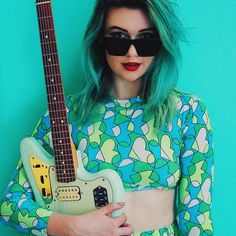 a woman with green hair and sunglasses holding an electric guitar