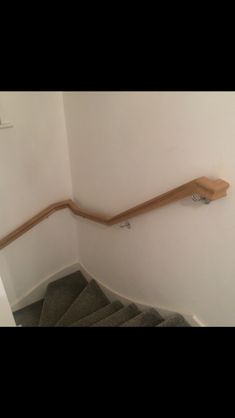 a wooden handrail on the side of a white wall next to a stair case