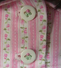 two white buttons are attached to a pink and green striped shirt with flowers on it