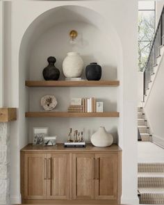 a living room with some shelves and vases on top of the shelf next to stairs