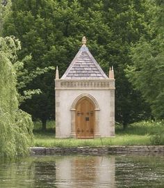 a small white building sitting on top of a lake next to a lush green forest