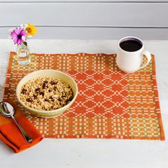 a bowl of oatmeal next to a cup of coffee on an orange placemat