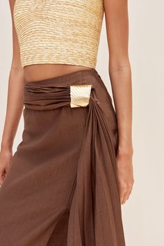 The Caroline Skirt reinvents the classic silhouette with texture and draping. A pleated waist detail wraps from the back of the skirt to the front. The warping is secured by a gold-toned, brushed brass shell-like hardware. The pleated fabric that drapes from the shell hardware adds movement and creates a high slit with an irregular hemline. Pink Wrap Skirt, Draping Skirt, Divided Skirt, Silk Wrap Skirt, Brass Shell, Boujee Outfits, Textured Skirt, Future Style