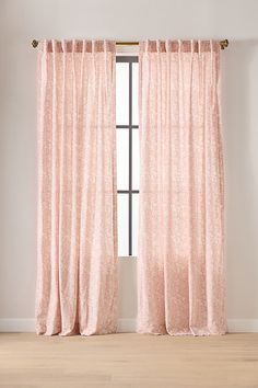 a pink curtain hanging in front of a window with white walls and wooden flooring