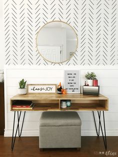 a desk with a mirror, stool and plant on it in front of a white wall