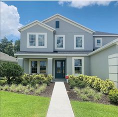 a house that is in the grass with bushes and flowers on the side walk way