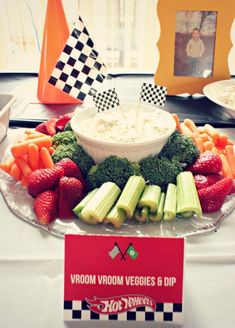 a plate with veggies and dip surrounded by strawberries, celery, broccoli