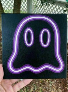 a hand holding up a black and purple sticker with a ghost face on it