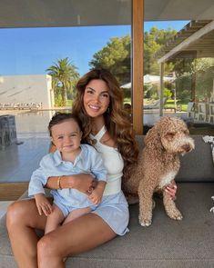 a woman sitting on top of a couch next to a brown dog and a little boy